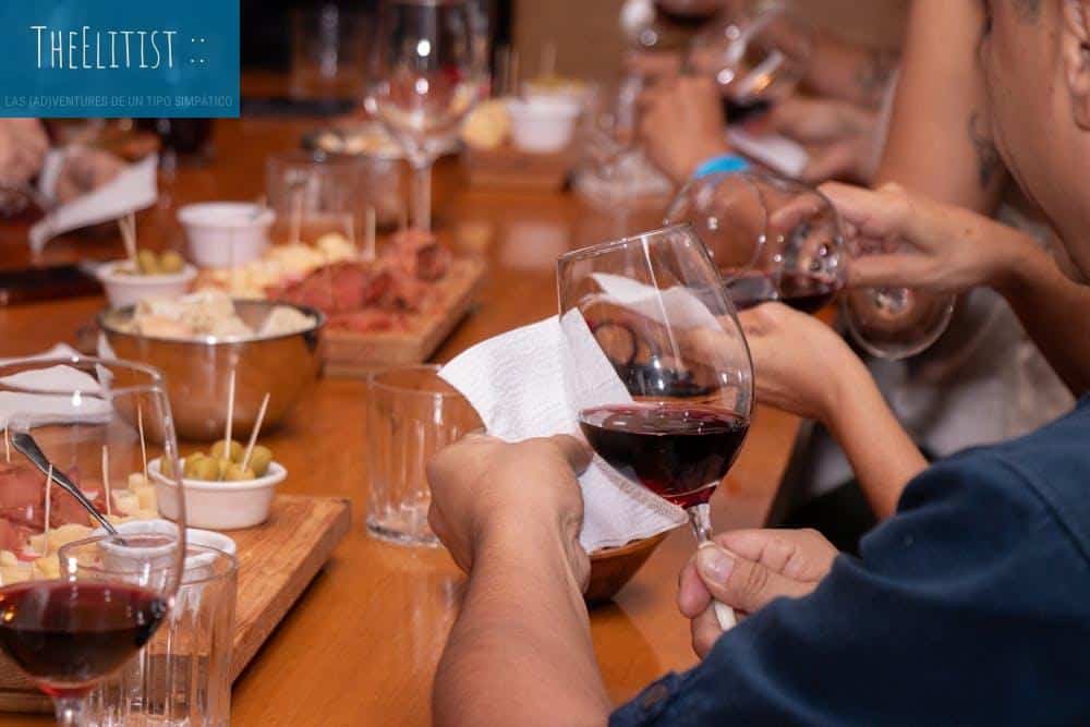 Close-up of people's hands holding wine glasses at a wine tasting event with snacks on a wooden table.