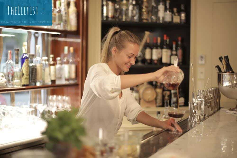 A cheerful bartender pours wine into a glass at an elegant bar counter.