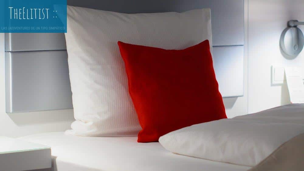 Stylish bedroom setup with a bold red accent pillow on a white bed, showcasing modern interior aesthetics.